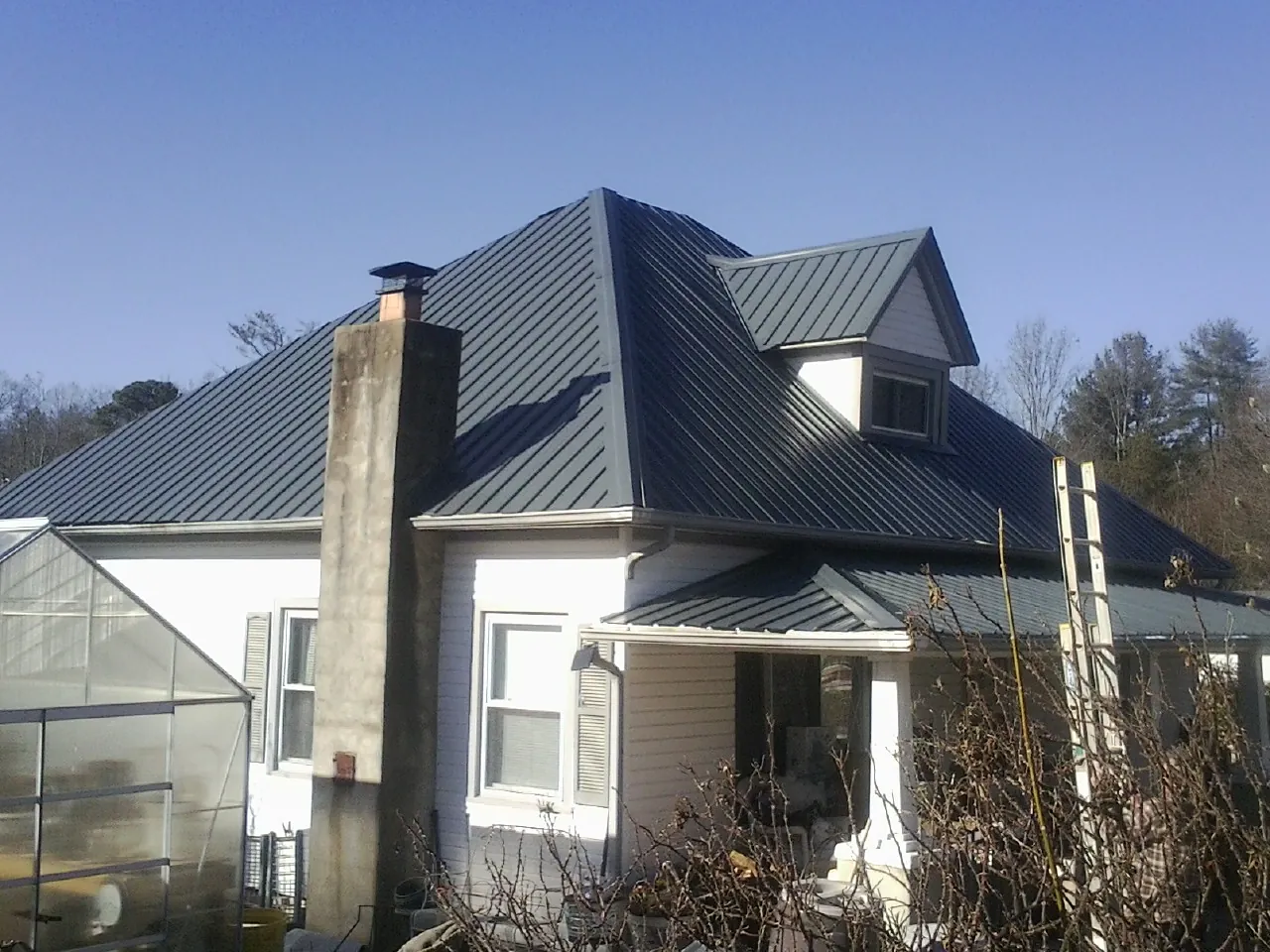 Dark blue standing seam metal roof on a white farmhouse with dormer — Slate & Tile Roof Repair by Roofing Brothers in Creekside