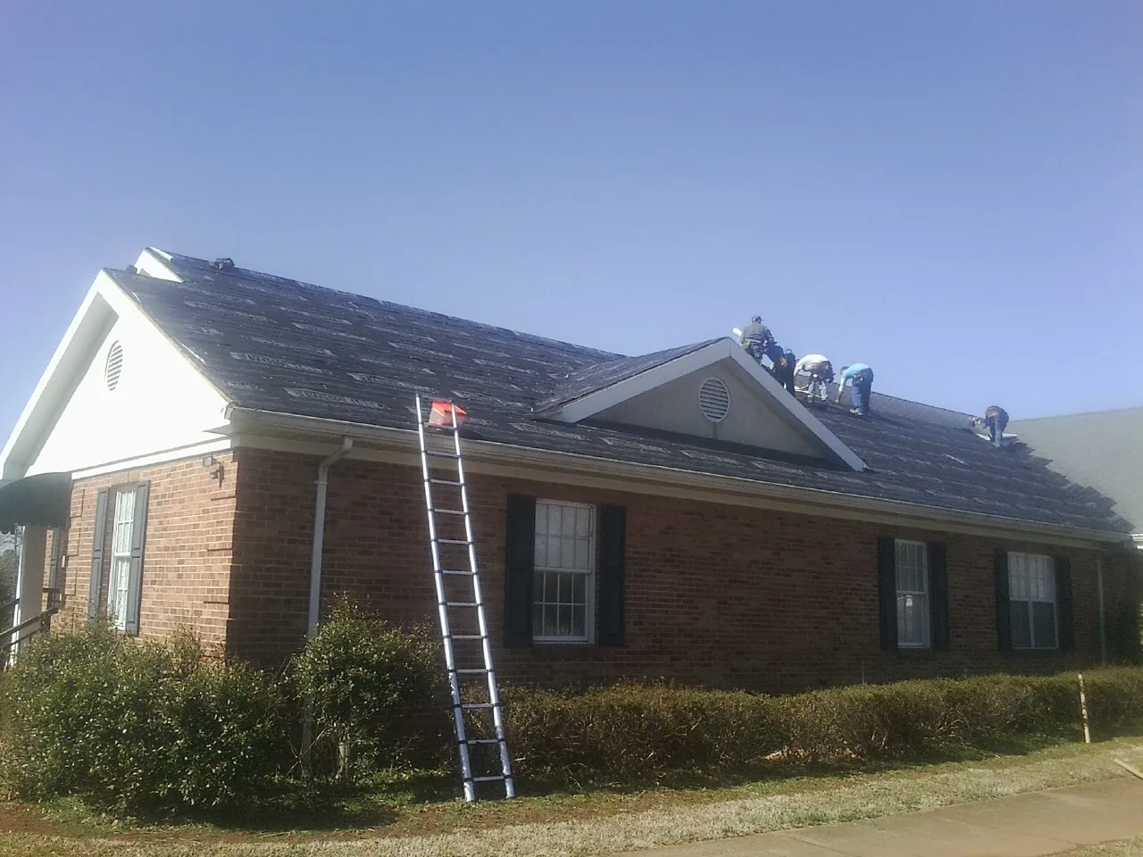 Crew tearing shingles off a brick ranch roof with a ladder set — Emergency Roof Repair work by our crew in Creekside