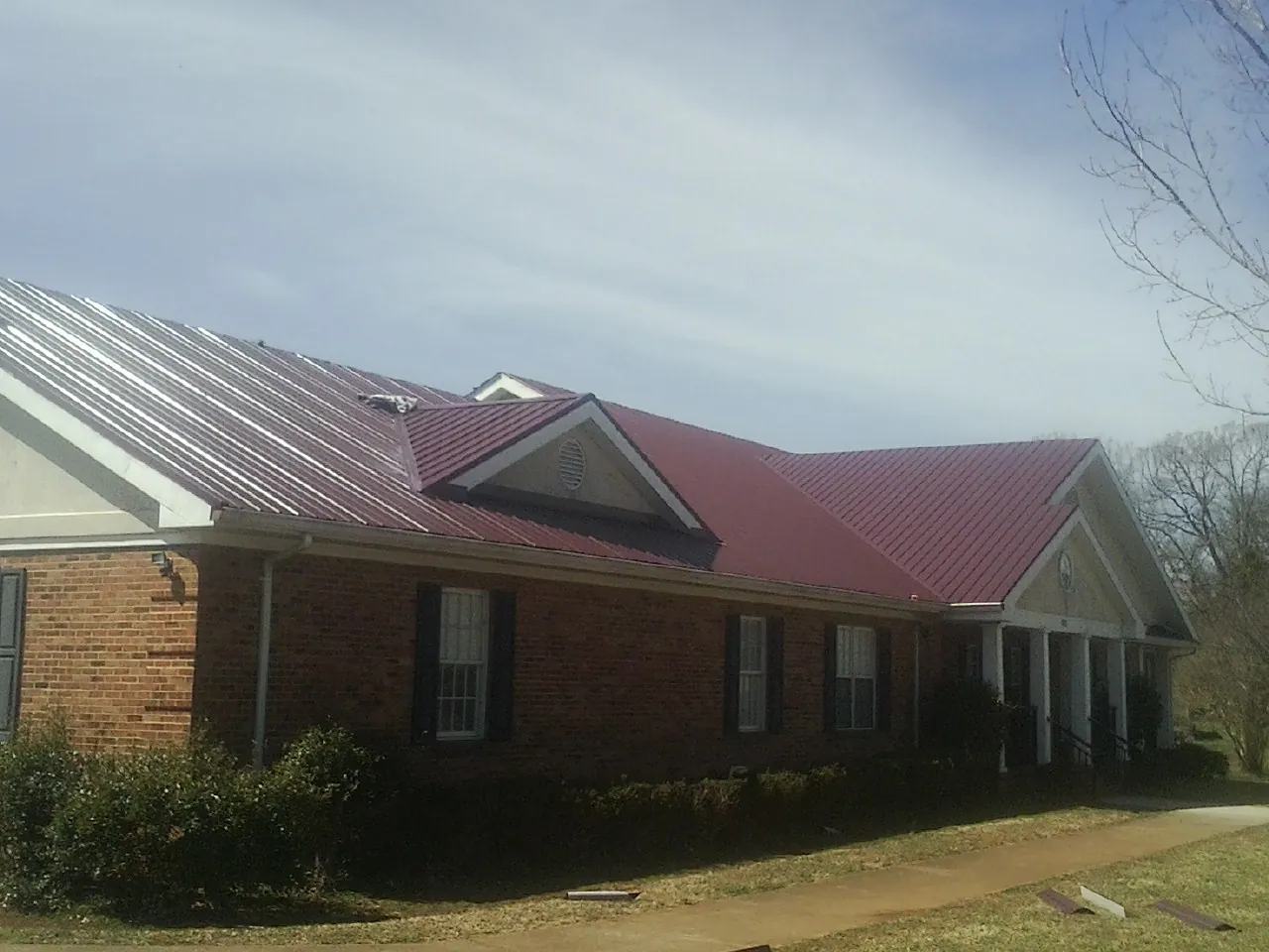 Red metal roof with gabled entries on a long brick building, from a Hail Damage Roof Repair job in Creekside