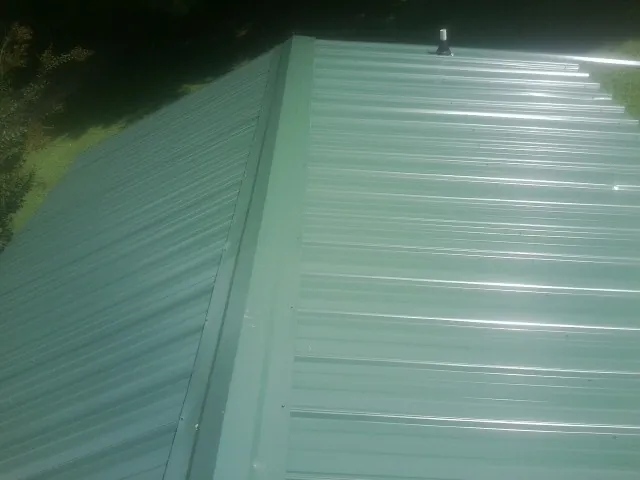 New green metal panels meeting at the ridge of a roof — Flat Roof Repair work by our crew in Creekside