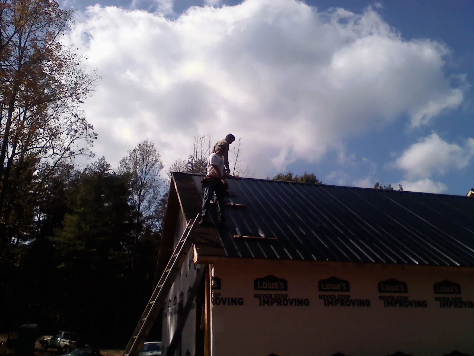 Roofer fastening dark metal panels high against a cloudy sky, from a Roof Inspection job in Creekside