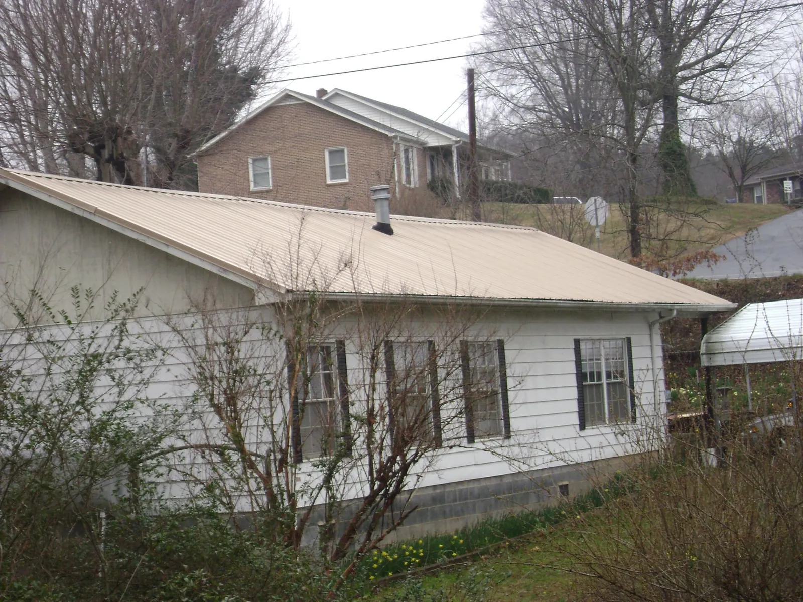 Tan metal roof on a white sided house set into a hillside — Commercial Roofing by Roofing Brothers in Creekside