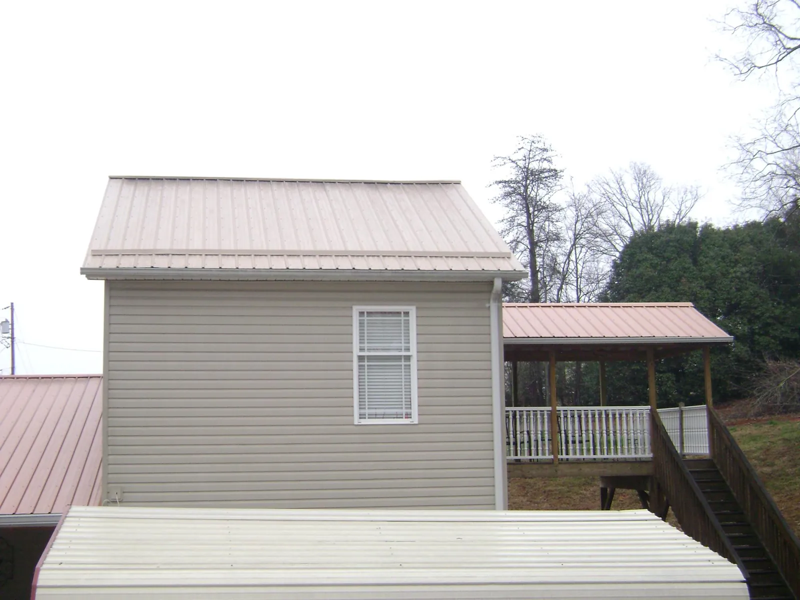 Tan metal roofs on a two story addition and attached porch, from a Roof Replacement job in Creekside
